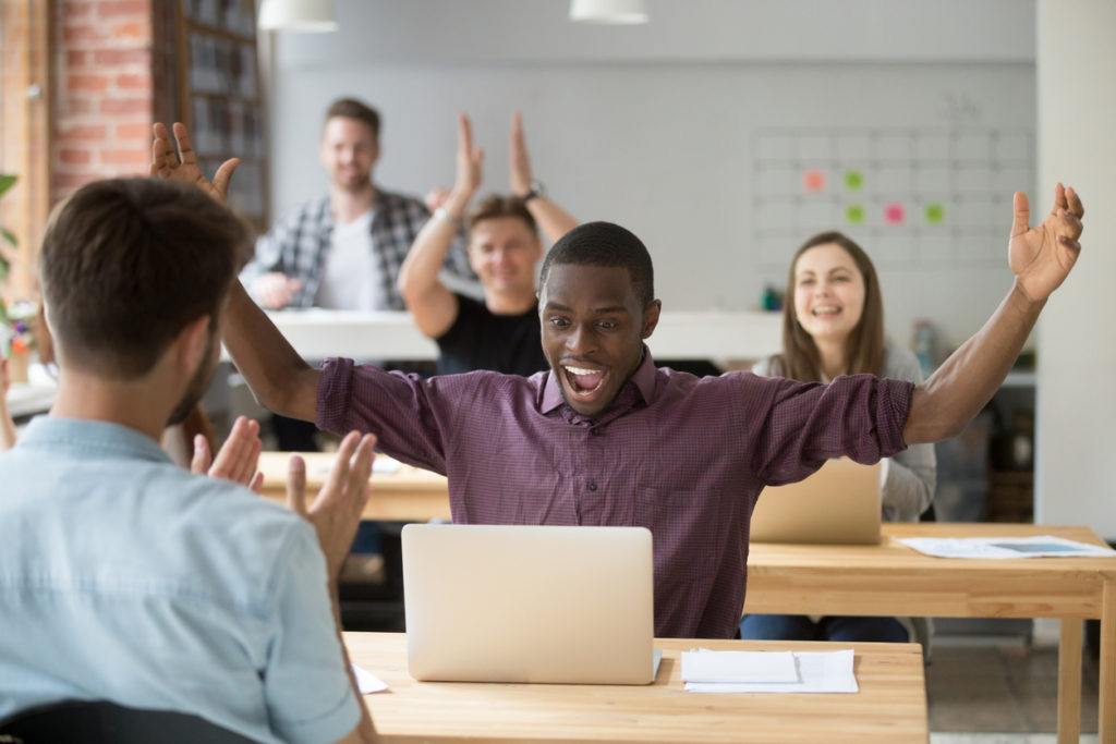 employee excited about online win, coworking team congratulating colleague