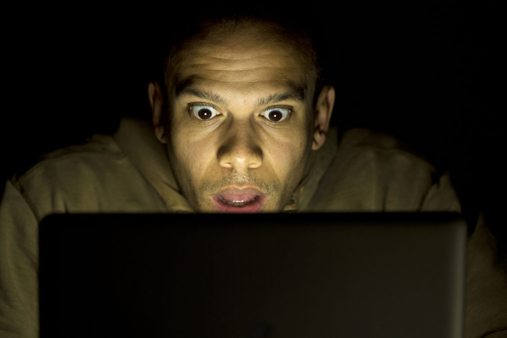 Shocked looking man using his laptop at night