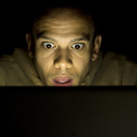 Shocked looking man using his laptop at night