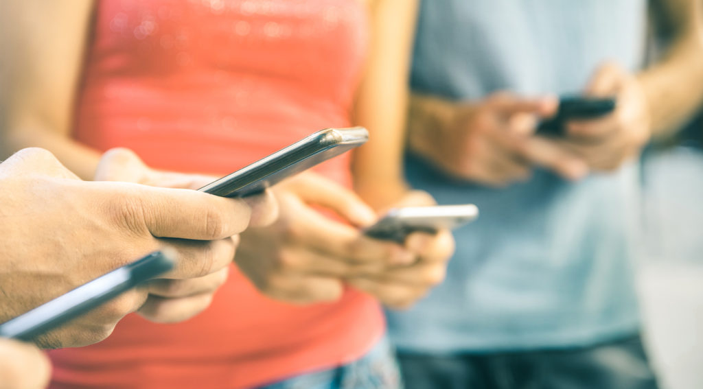 Multicultural friends using smartphone outdoors - People hands addicted by mobile smart phone - Technology concept with connected men and women - Shallow depth of field on bright vintage filtered tone