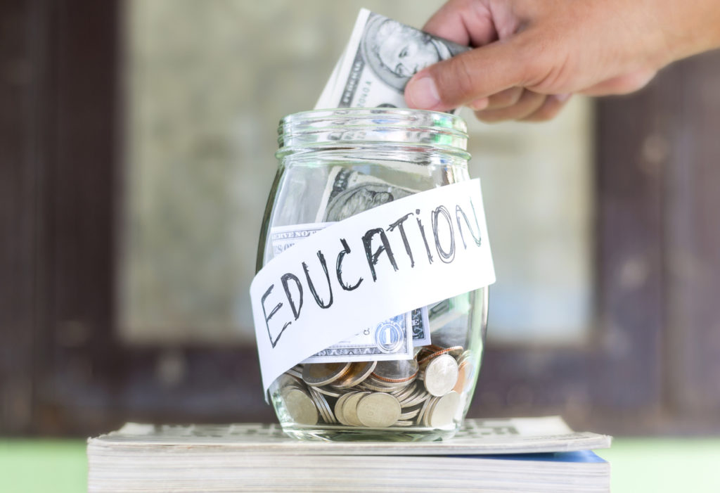 Coins and banknote in a glass jar placed on the textbook.