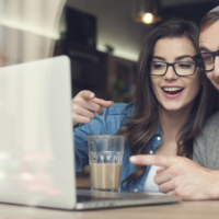 Man and woman smiling at computer screen in coffee shop