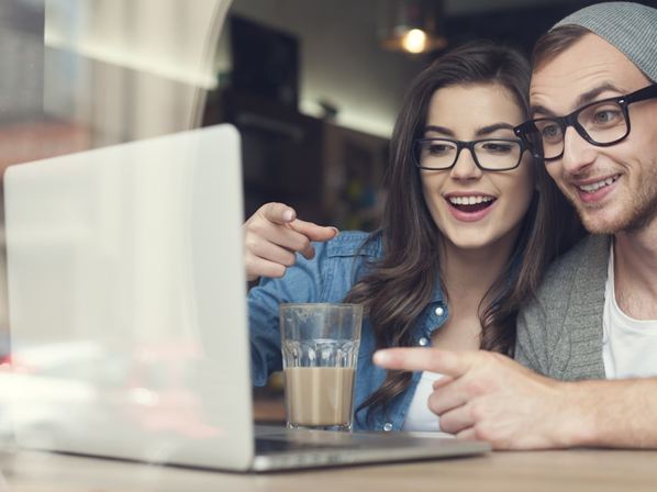 Man and woman smiling at computer screen in coffee shop